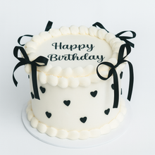 Afbeelding in Gallery-weergave laden, witte botercreme taart in vintage stijl met zwarte strikjes van lint, kleine zwarte hartjes aan de zijkant en bovenop een eetbare print met Happy Birthday erop.
